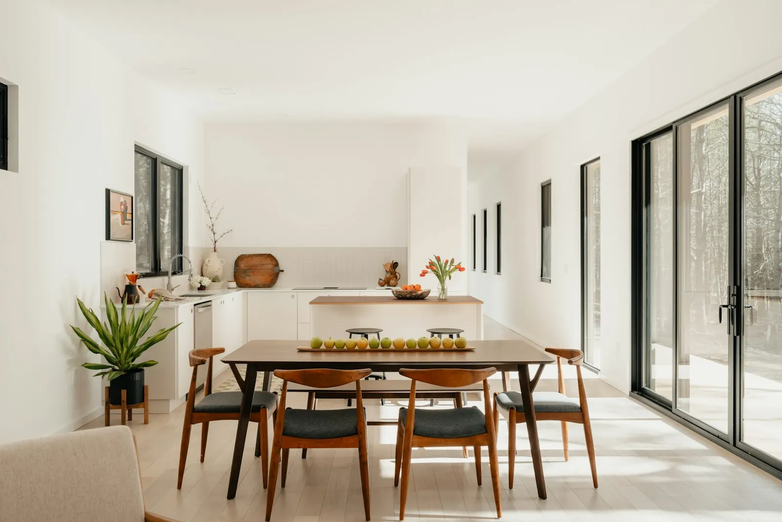 Sala de refeições luminosa de uma casa, com mesa de madeira e cadeiras junto a janelas amplas